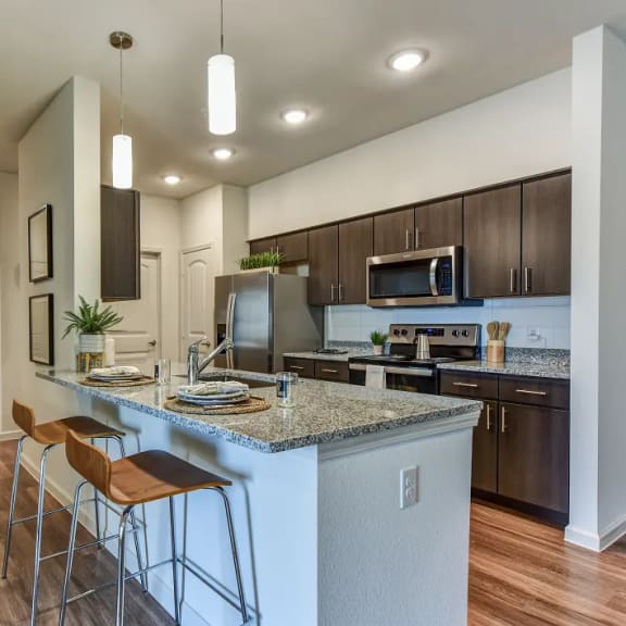 Thumbnail 2 of 11 Open concept kitchen with island seating and pendant lights at High Point Preserve Apartments, Texas