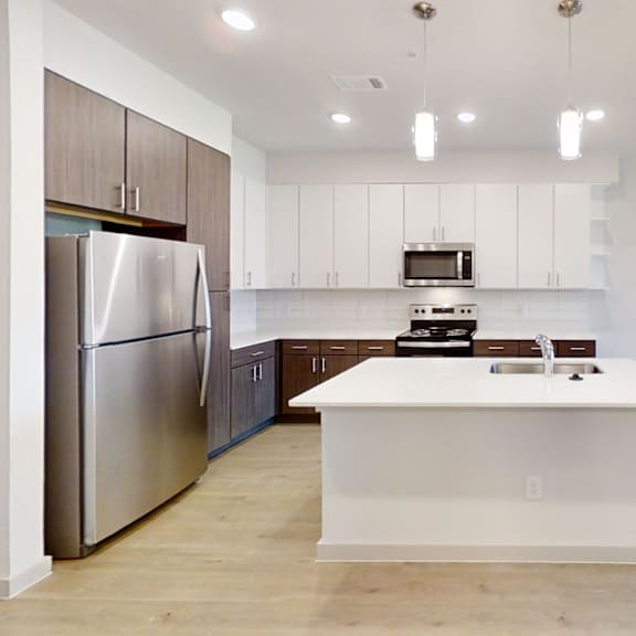 Thumbnail 3 of 10 A modern kitchen with stainless steel appliances and a central island. at ThreeTwenty at the Vybe Apartments, Kyle, TX