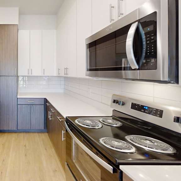 Thumbnail 4 of 10 A modern kitchen with stainless steel appliances and wooden cabinets. at ThreeTwenty at the Vybe Apartments, Kyle, 78640
