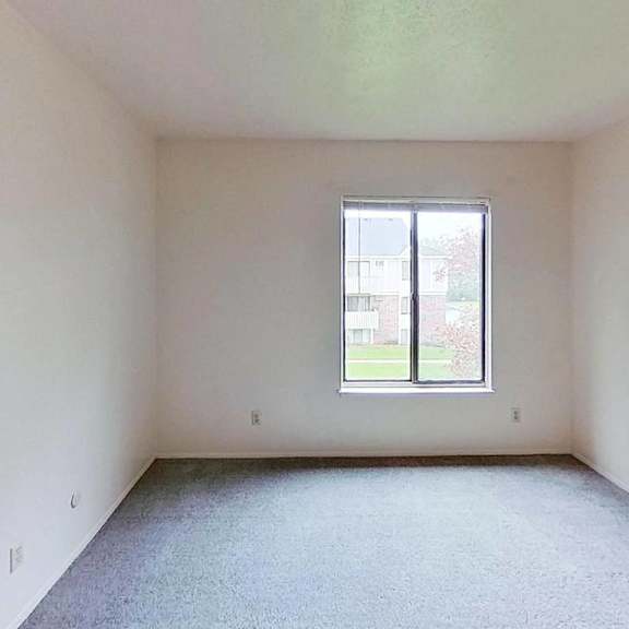 Thumbnail 12 of 12 A bedroom with a large window and carpeted floor at Briarwood Apartments in Benton Harbor, MI