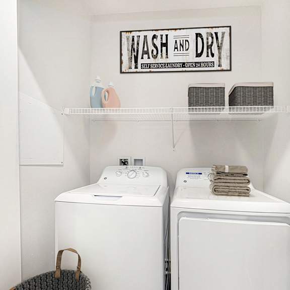 Thumbnail 6 of 8 A laundry area with a washer and dryer and a shelf above them at Andover Pointe Apartment Homes, La Vista, NE, 68138