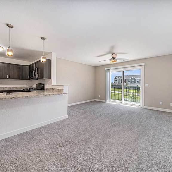 Thumbnail 3 of 9 A spacious living room with a kitchen area and a ceiling fan at Andover Pointe Apartment Homes, La Vista, NE, 68138