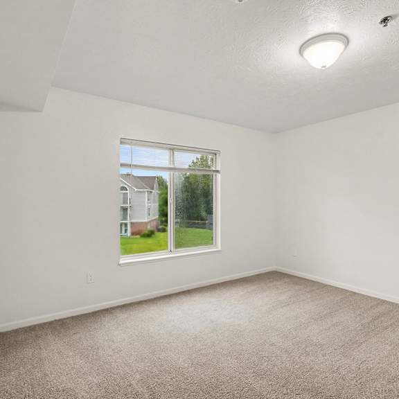 Thumbnail 16 of 22 A room with a carpeted floor and a window showing a view of a house.