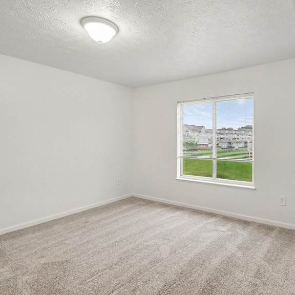 Thumbnail 17 of 22 A room with a carpeted floor and a window showing a view of a house.