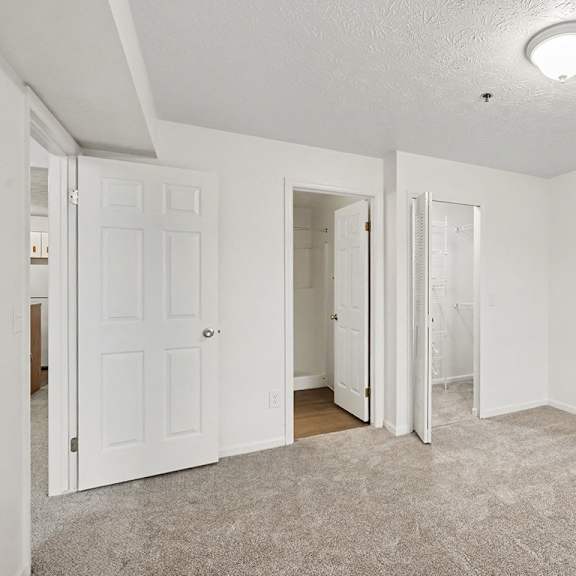 Thumbnail 19 of 22 A room with white walls and carpeted floor with three doors.