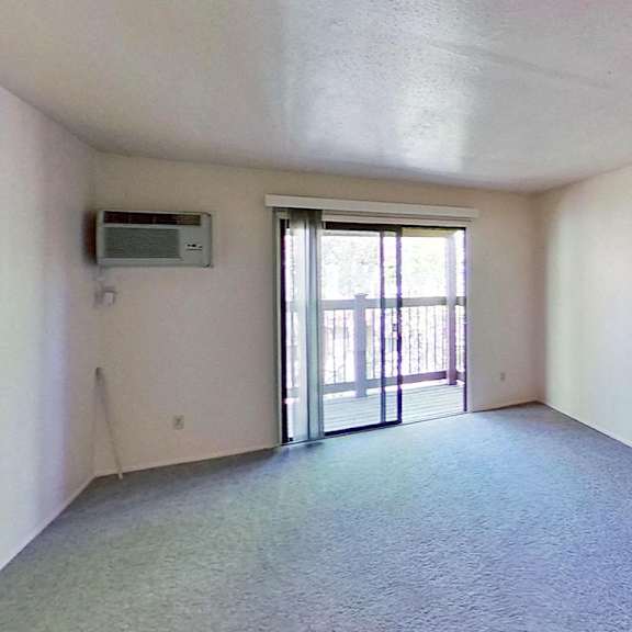Thumbnail 5 of 10 A living room with a carpeted floor and a sliding glass door leading to a balcony at Briarwood Apartments in Benton Harbor, MI