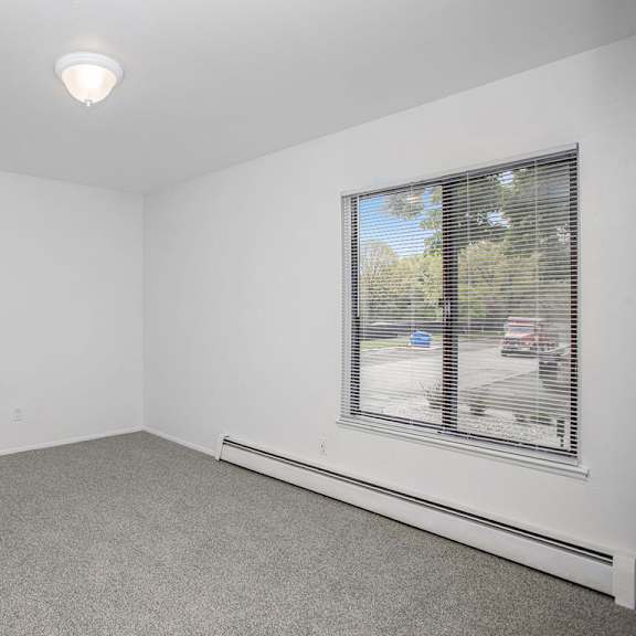Thumbnail 11 of 13 A bedroom with a large window and a grey carpet at Brookside Apartments, Springfield