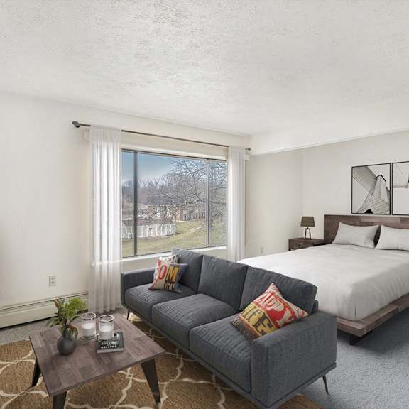 Thumbnail 4 of 11 A bedroom and living room area with a bed, couch, and a large window at Brookside Apartments, Springfield