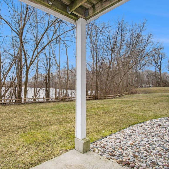 Thumbnail 4 of 16 a patio with a view of a pond and trees at Canal 2 Apartments in Lansing, MI