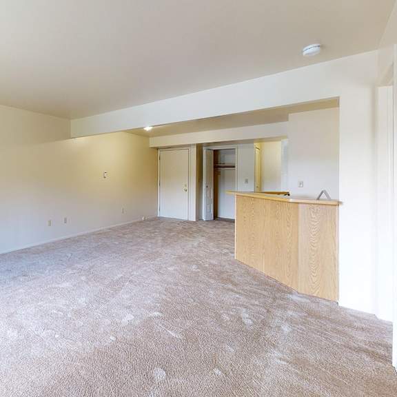 Thumbnail 4 of 8 A large, empty living room with a carpeted floor at Canal Club Apartments, Lansing, 48917