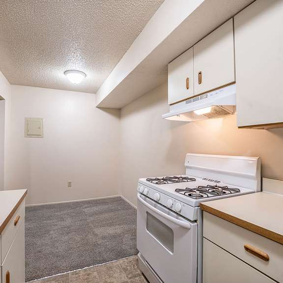 Thumbnail 10 of 14 A kitchen with a white stove leading to a dining area at Concord Place Apartments, Kalamazoo, MI, 49009