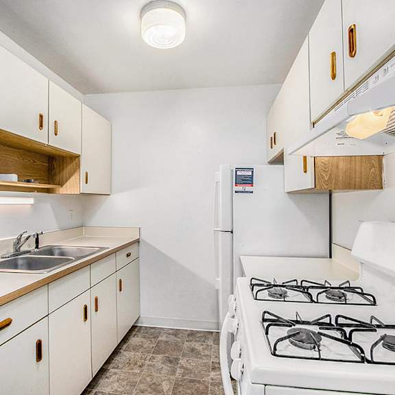 Thumbnail 9 of 15 A galley-style kitchen with a stove, refrigerator, and sink at Concord Place Apartments, Kalamazoo, MI