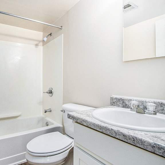 Thumbnail 12 of 15 A white, upgraded bathroom with a toilet, sink, and bathtub at Concord Place Apartments, Kalamazoo, MI