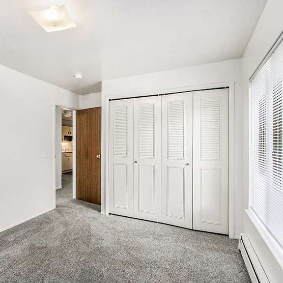 Thumbnail 14 of 15 A bedroom with a large window, closet and grey carpet at Concord Place Apartments, Kalamazoo, MI
