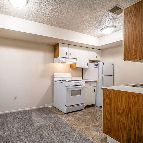 Thumbnail 7 of 14 A dining area and kitchen with white appliances and wooden cabinets at Concord Place Apartments, Kalamazoo, MI, 49009