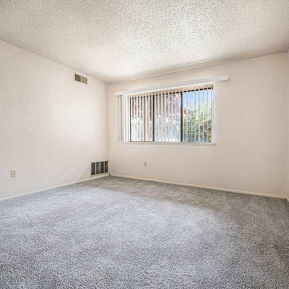 Thumbnail 5 of 14 A living room with a carpeted floor and a window with blinds at Concord Place Apartments, Kalamazoo, MI, 49009