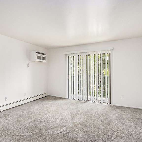 Thumbnail 3 of 15 A living room with a slider to a balcony, blinds, and a carpeted floor at Concord Place Apartments, Kalamazoo, MI