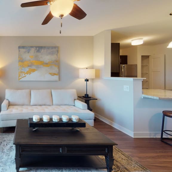 Thumbnail 6 of 15 A modern living room with a white couch and ceiling fan at Copper Creek Apartment Homes, Maize, KS, 67101