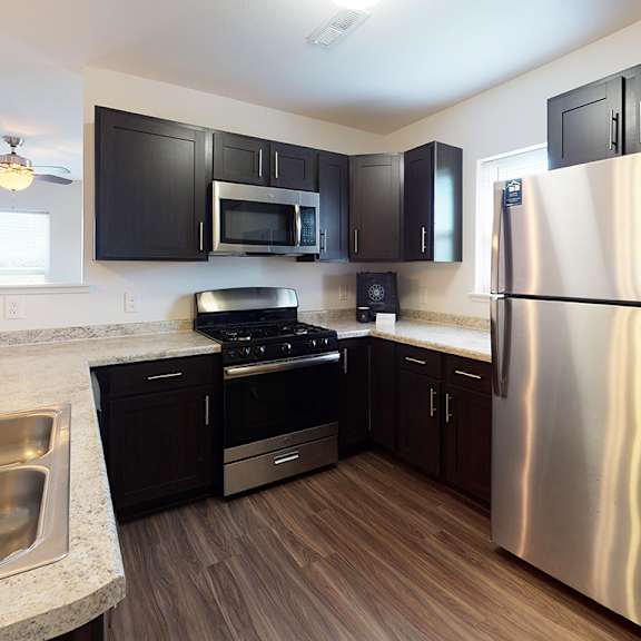 Thumbnail 6 of 10 A modern kitchen with a stainless steel refrigerator, sink, and dark brown cabinets at Copper Creek Apartment Homes, Maize