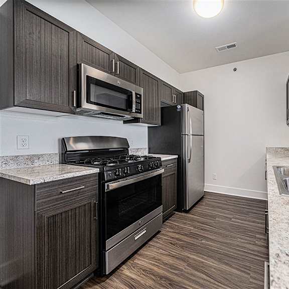 Thumbnail 8 of 14 A kitchen with dark wood cabinets and stainless steel appliances at Copper Creek Apartment Homes, Maize