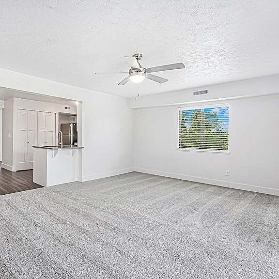 Thumbnail 6 of 13 A living room with a ceiling fan and carpeted floor at The Crossings Apartments in Grand Rapids, MI