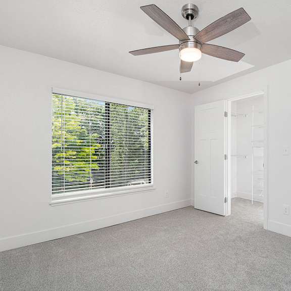 Thumbnail 15 of 16 A bedroom with a ceiling fan and a window with blinds at The Crossings Apartments, Grand Rapids, 49508