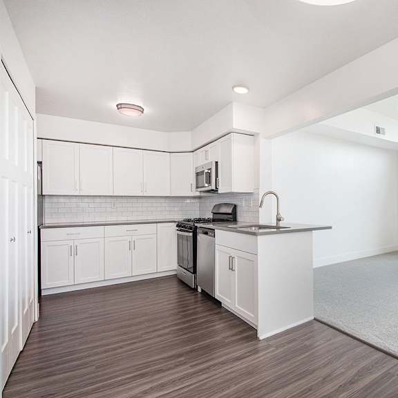 Thumbnail 3 of 16 A kitchen with white cabinets and a living room with cathedral ceiling at The Crossings Apartments, Grand Rapids