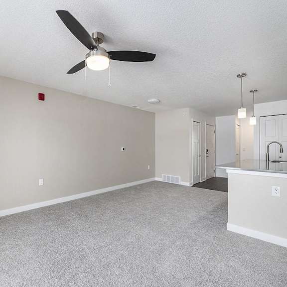 Thumbnail 7 of 14 A living room with a ceiling fan and a carpeted floor at Eagle Ridge Apartment Homes, Traverse City, Michigan