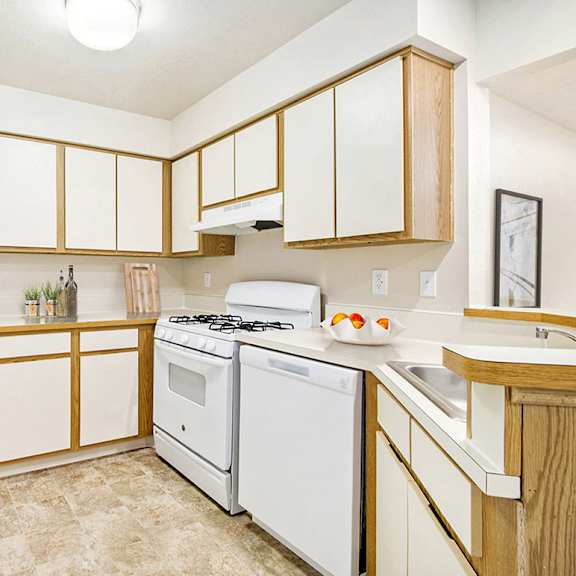 Thumbnail 3 of 7 A kitchen with white appliances and wooden cabinets at Emerald Park Apartments, Kalamazoo, Michigan
