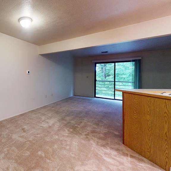 Thumbnail 3 of 10 A living room with plush carpeting and a slider to a private balcony at Emerald Park Apartments, Kalamazoo