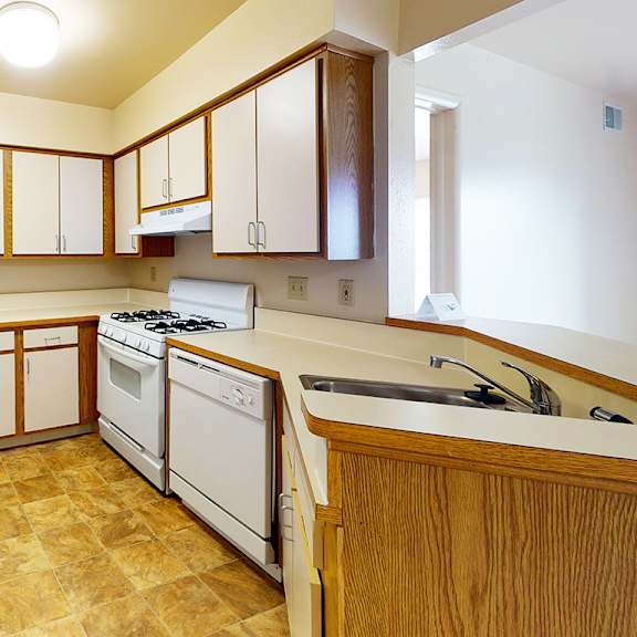 Thumbnail 9 of 17 A kitchen with white appliances and wooden cabinets at Emerald Park Apartments, Kalamazoo, Michigan