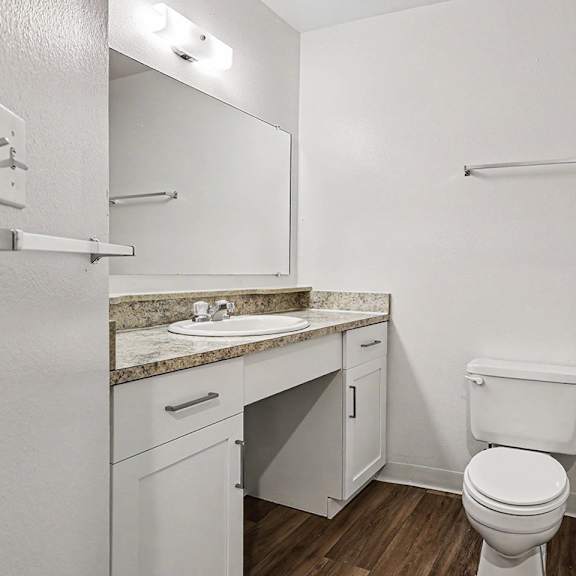 Thumbnail 10 of 17 A white bathroom with a toilet, sink, and mirror at Emerald Park Apartments, Kalamazoo, Michigan