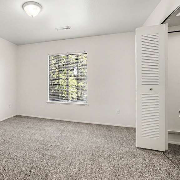 Thumbnail 15 of 17 A bedroom with a window and a door to a walk-in closet at Emerald Park Apartments, Kalamazoo, Michigan