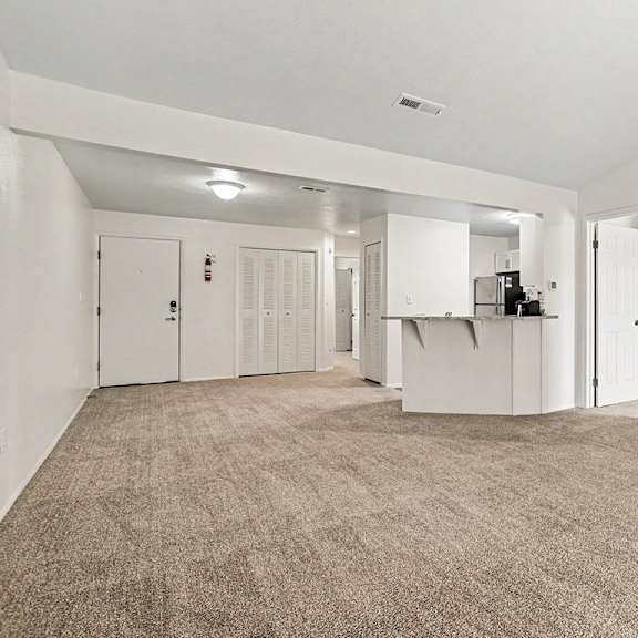 Thumbnail 6 of 17 A large, empty living room with a high ceiling and carpeted flooring at Emerald Park Apartments, Kalamazoo, Michigan