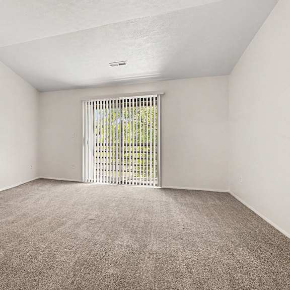 Thumbnail 4 of 17 A living room with a carpeted floor and a sliding glass door to a balcony at Emerald Park Apartments, Kalamazoo, Michigan