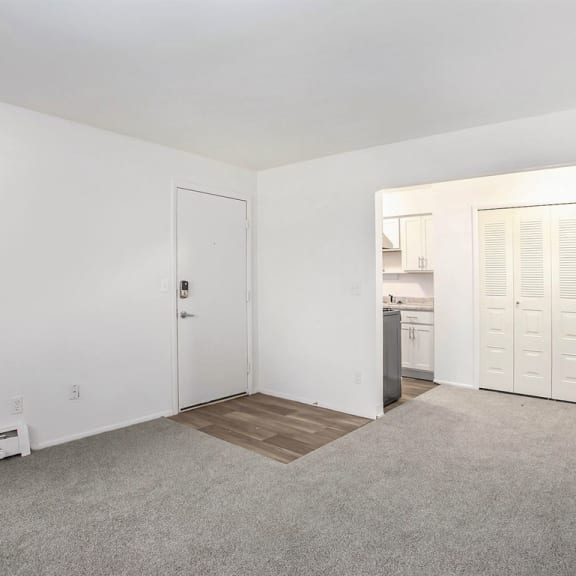 Thumbnail 7 of 17 an empty living room with a kitchen in the background at Fairlane Apartments in Springfield, Michigan 49037
