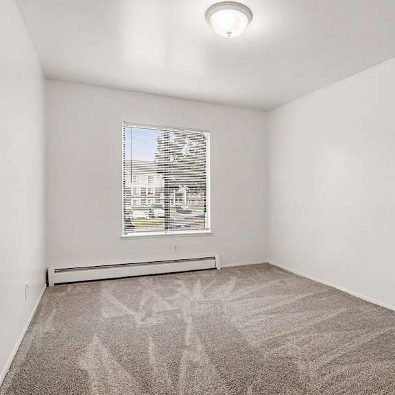 Thumbnail 16 of 17 Empty carpeted room with window and baseboard heater at Fairlane Apartments, Springfield, 49037