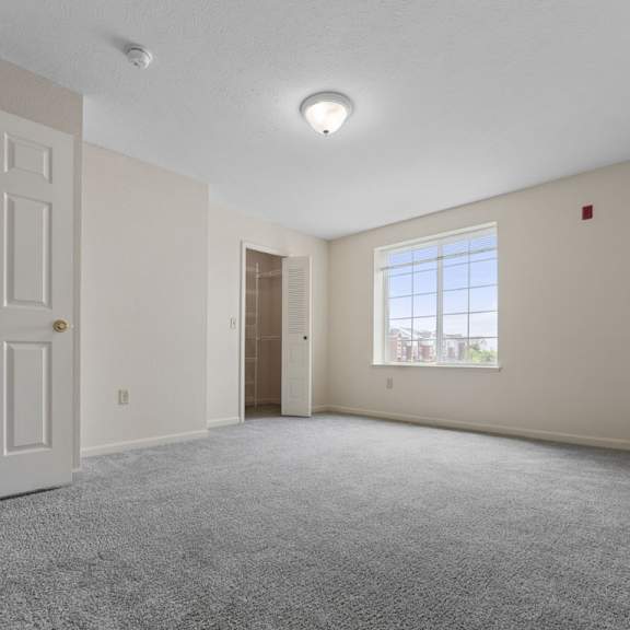 Thumbnail 13 of 18 A bedroom with a carpeted floor, large window, and a walk-in closet at Fieldstream Apartment Homes, Iowa