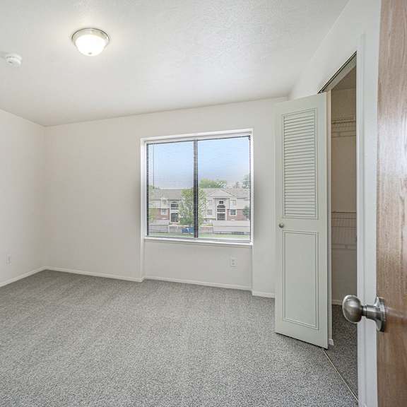 Thumbnail 11 of 12 A large bedroom with a carpeted floor and a window at Foxwood and The Hermitage in Portage, MI