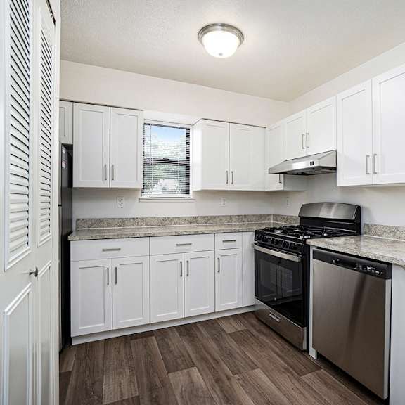 Thumbnail 6 of 12 A kitchen with white cabinets and a stainless steel dishwasher and oven at Foxwood and The Hermitage in Portage, MI