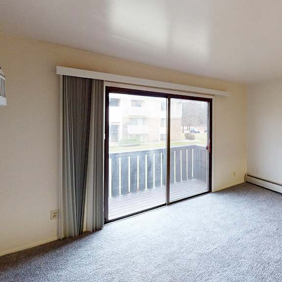 Thumbnail 5 of 14 A living room with plush carpet and a sliding glass door at Glen Oaks Apartments, Michigan, 49442