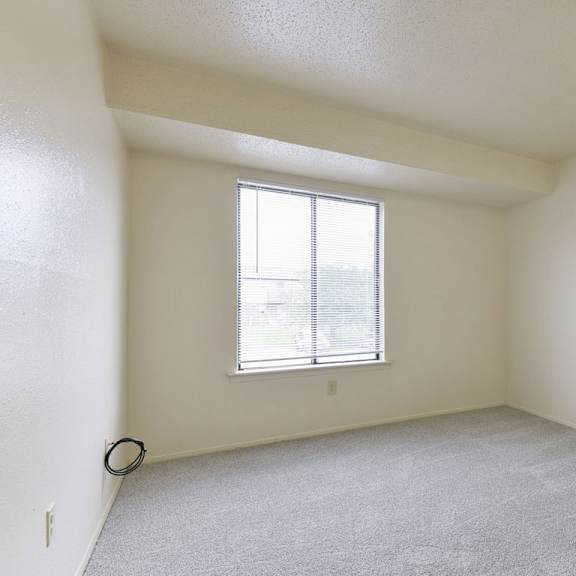 Thumbnail 11 of 12 A bedroom with a large window and a carpeted floor at Granada Apartments, Jackson, 49202