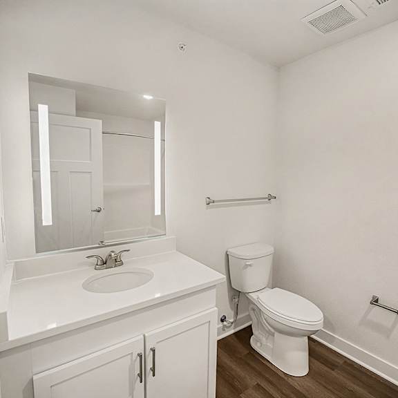 Thumbnail 14 of 19 A white bathroom with a toilet, sink, and mirror at The Grove Apartment Homes in Lincoln, NE