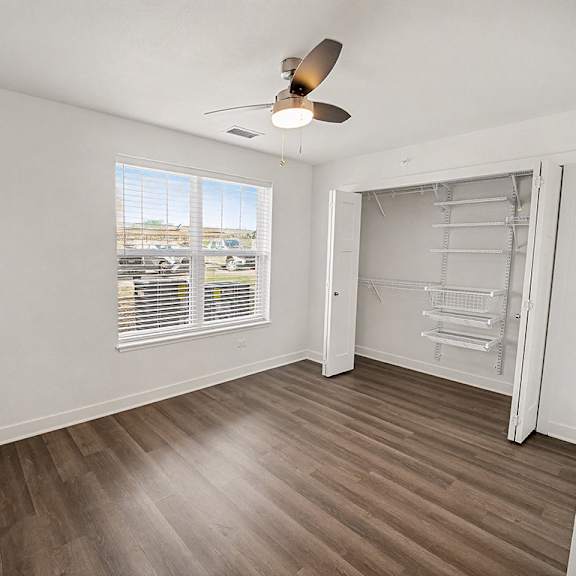 Thumbnail 17 of 19 A spacious bedroom with a ceiling fan and a large window with blinds at The Grove Apartment Homes in Lincoln, NE