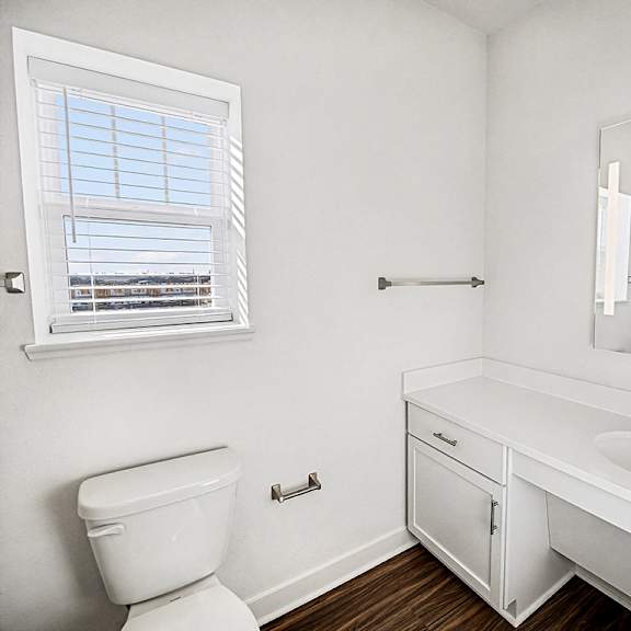 Thumbnail 9 of 13 A white bathroom with a toilet, sink, mirror and a window at The Grove Apartment Homes in Lincoln, NE