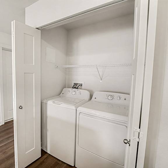 Thumbnail 13 of 19 A white, full-size washing machine and dryer in a small laundry area at The Grove Apartment Homes in Lincoln, NE