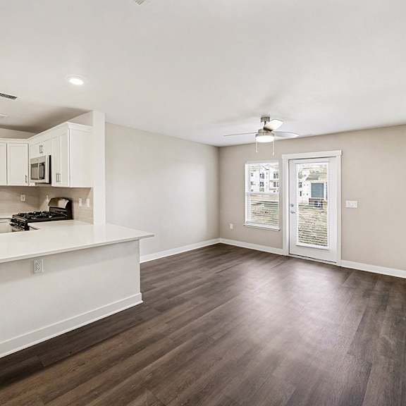 Thumbnail 4 of 19 A kitchen with white cabinets and a living room with a ceiling fan at The Grove Apartment Homes in Lincoln, NE