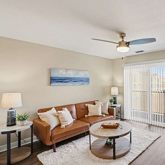 Thumbnail 5 of 19 A living room with a brown couch, a slider to a balcony, and a ceiling fan at The Grove Apartment Homes, Nebraska