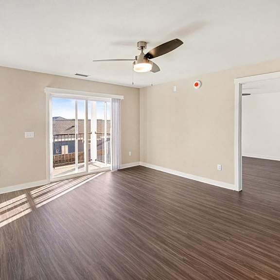 Thumbnail 3 of 14 A living room with a ceiling fan and sliding glass doors to a balcony at The Grove Apartment Homes in Lincoln, NE