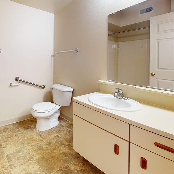 Thumbnail 10 of 13 A bathroom with a toilet, sink, and mirror at Gull Prairie/Gull Run Apartments and Townhomes in Kalamazoo, MI